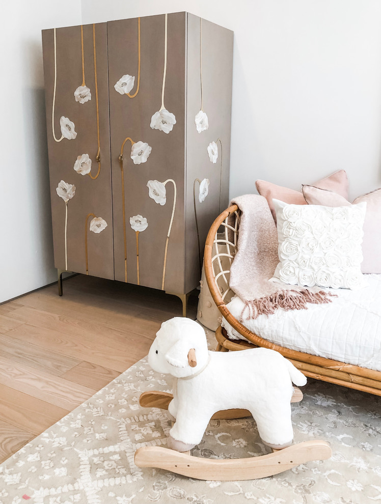 Photo of a mid-sized transitional nursery for girls in New York with white walls, bamboo floors and brown floor.