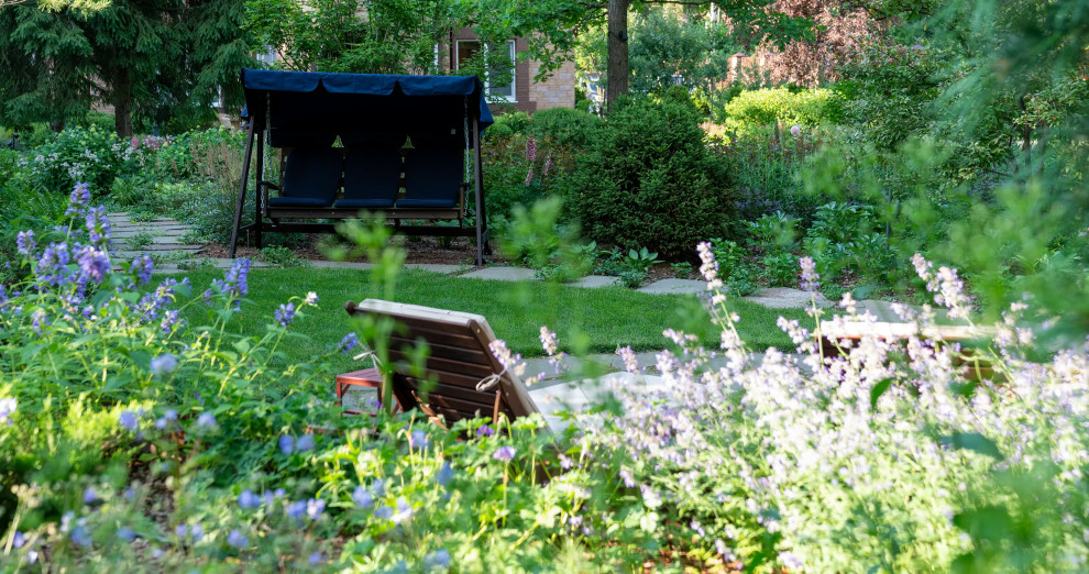 Idée de décoration pour un grand jardin arrière champêtre l'été avec un massif de fleurs, une exposition partiellement ombragée, des pavés en pierre naturelle et une clôture en métal.