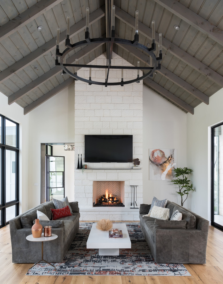 Inspiration for a country living room in Austin with white walls, medium hardwood floors, a standard fireplace, a stone fireplace surround, a wall-mounted tv and brown floor.