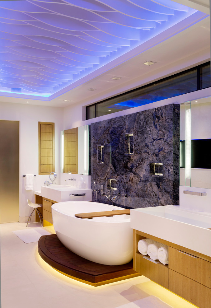 Inspiration for a large contemporary master bathroom in Houston with flat-panel cabinets, light wood cabinets, a freestanding tub, stone slab, blue walls, a trough sink, porcelain floors and solid surface benchtops.