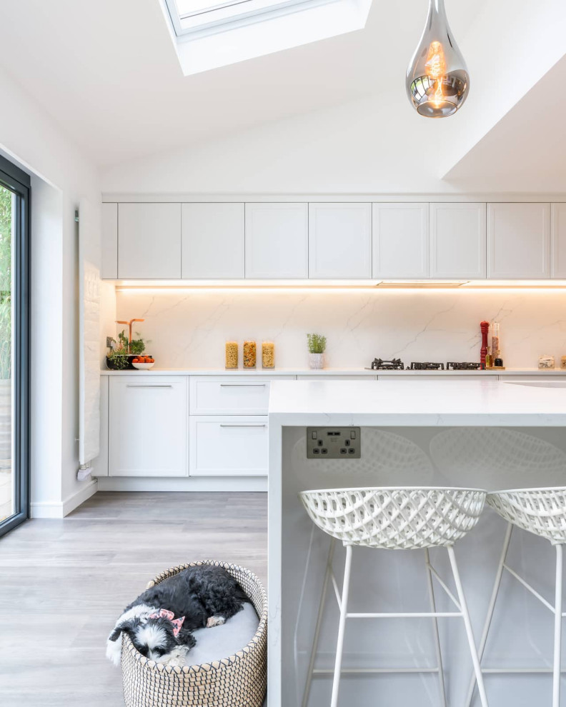 Large l-shaped eat-in kitchen in Sussex with a single-bowl sink, shaker cabinets, white cabinets, quartzite benchtops, white splashback, light hardwood floors, with island, brown floor, white benchtop and recessed.