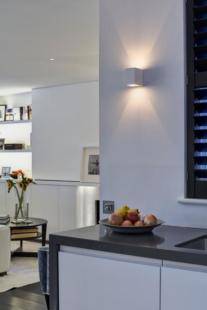 Small contemporary l-shaped eat-in kitchen in London with an undermount sink, flat-panel cabinets, white cabinets, marble benchtops, black appliances, dark hardwood floors and a peninsula.