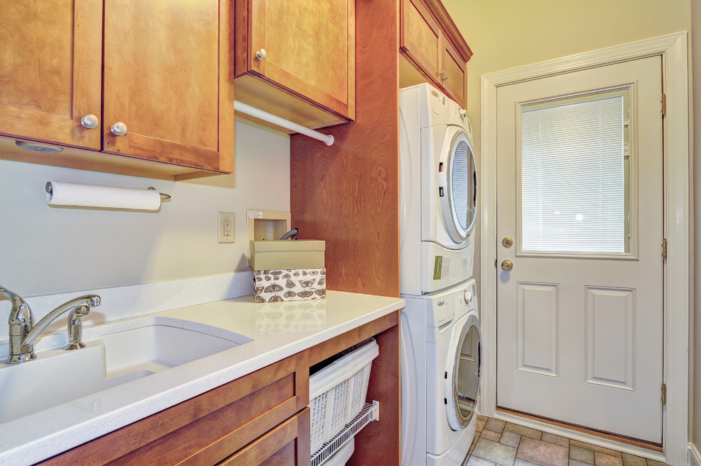 Inspiration for a small traditional galley utility room in Philadelphia with recessed-panel cabinets, medium wood cabinets, yellow walls, ceramic floors, a stacked washer and dryer and a drop-in sink.