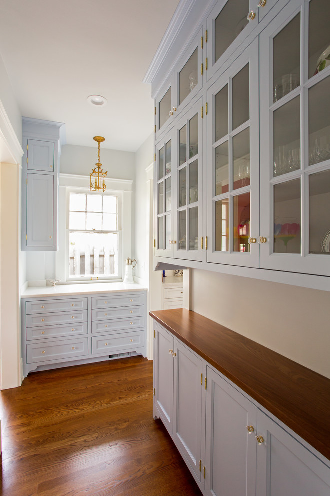 Inspiration for a mid-sized timeless galley medium tone wood floor and brown floor enclosed kitchen remodel in Cleveland with a farmhouse sink, flat-panel cabinets, white cabinets, granite countertops, white backsplash, subway tile backsplash, paneled appliances and no island