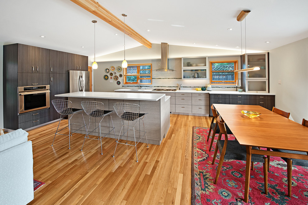 Inspiration for a midcentury l-shaped open plan kitchen in Denver with flat-panel cabinets, grey cabinets, grey splashback, subway tile splashback, stainless steel appliances, medium hardwood floors, with island, brown floor and white benchtop.