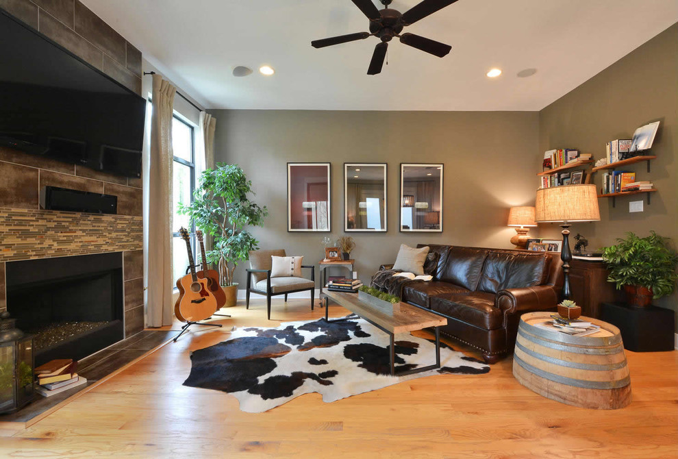 This is an example of a large industrial open concept living room in Austin with light hardwood floors, a standard fireplace, a stone fireplace surround, a wall-mounted tv and brown walls.