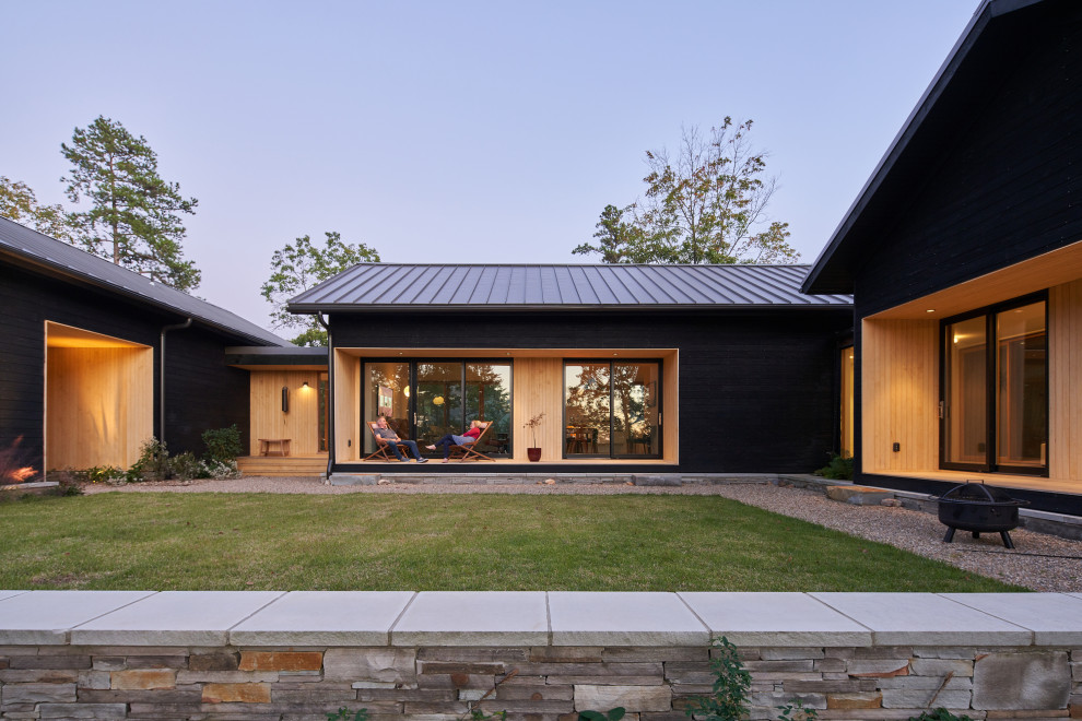 Esempio della villa nera moderna a un piano con rivestimento in pietra, tetto a capanna, copertura in metallo o lamiera, tetto grigio e pannelli sovrapposti