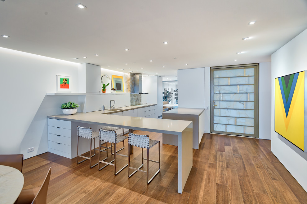 Contemporary l-shaped kitchen in Orange County with flat-panel cabinets, white cabinets, medium hardwood floors, a peninsula, brown floor and grey benchtop.