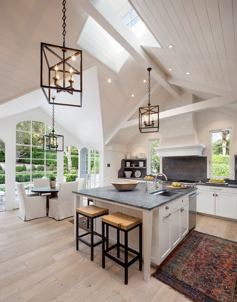 Traditional l-shaped eat-in kitchen in Santa Barbara with an undermount sink, recessed-panel cabinets, white cabinets, soapstone benchtops, grey splashback, stone slab splashback, stainless steel appliances, light hardwood floors and with island.