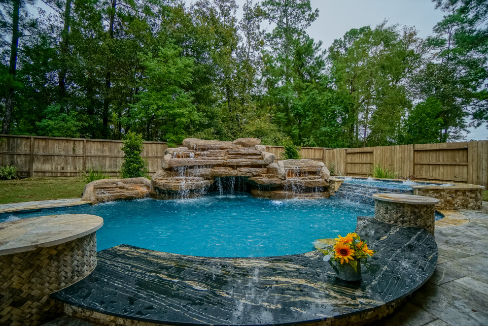 Inspiration for a large tropical backyard custom-shaped pool in Houston with natural stone pavers.