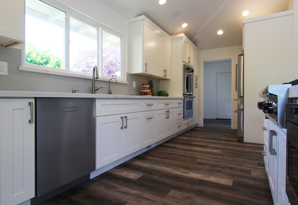 Open concept kitchen - large transitional single-wall vinyl floor and brown floor open concept kitchen idea with an undermount sink, shaker cabinets, white cabinets, quartz countertops, gray backsplash, ceramic backsplash, stainless steel appliances, an island and white countertops