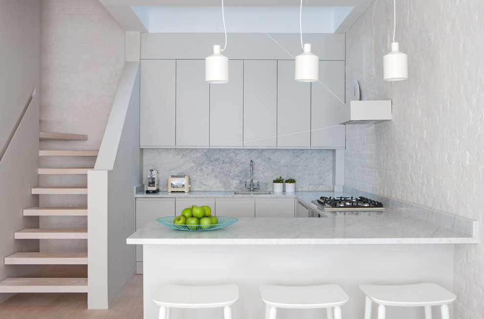 This is an example of a modern single-wall open plan kitchen in Copenhagen with flat-panel cabinets, grey cabinets, grey splashback, light hardwood floors, a peninsula, beige floor and grey benchtop.