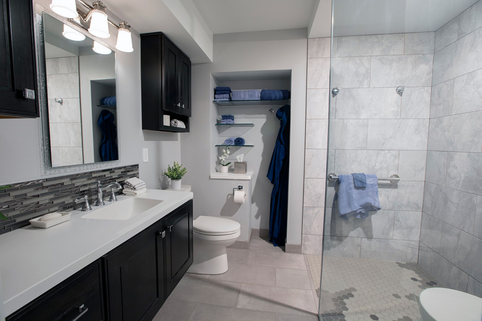 This is an example of a mid-sized transitional bathroom in Detroit with shaker cabinets, black cabinets, a curbless shower, a one-piece toilet, gray tile, an undermount sink, grey floor, a hinged shower door, white benchtops, a single vanity and a floating vanity.