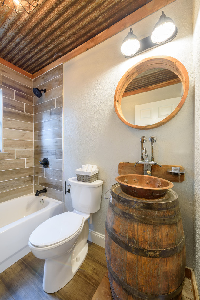 This is an example of a small country master bathroom in Dallas with a drop-in tub, a shower/bathtub combo, a two-piece toilet, grey walls, dark hardwood floors, a vessel sink, wood benchtops, brown floor, a sliding shower screen and brown benchtops.