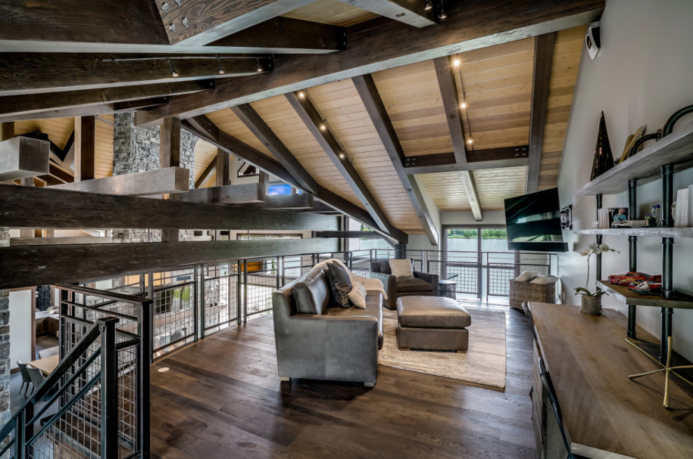 Photo of an expansive country loft-style family room in Seattle with grey walls, dark hardwood floors, no fireplace, a wall-mounted tv, black floor and exposed beam.