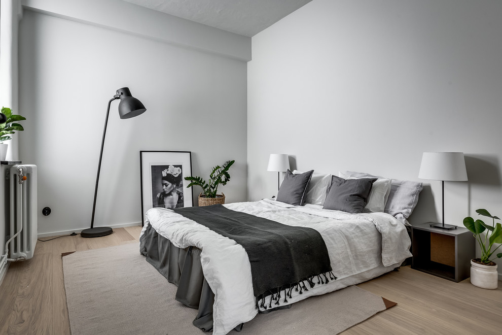 This is an example of a large scandinavian master bedroom in Stockholm with white walls, light hardwood floors and beige floor.