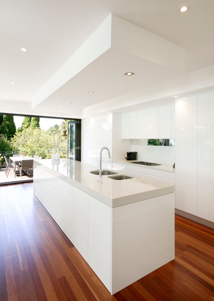 This is an example of a modern galley eat-in kitchen in Sydney with an undermount sink, flat-panel cabinets, white cabinets, quartz benchtops, white splashback, medium hardwood floors and with island.