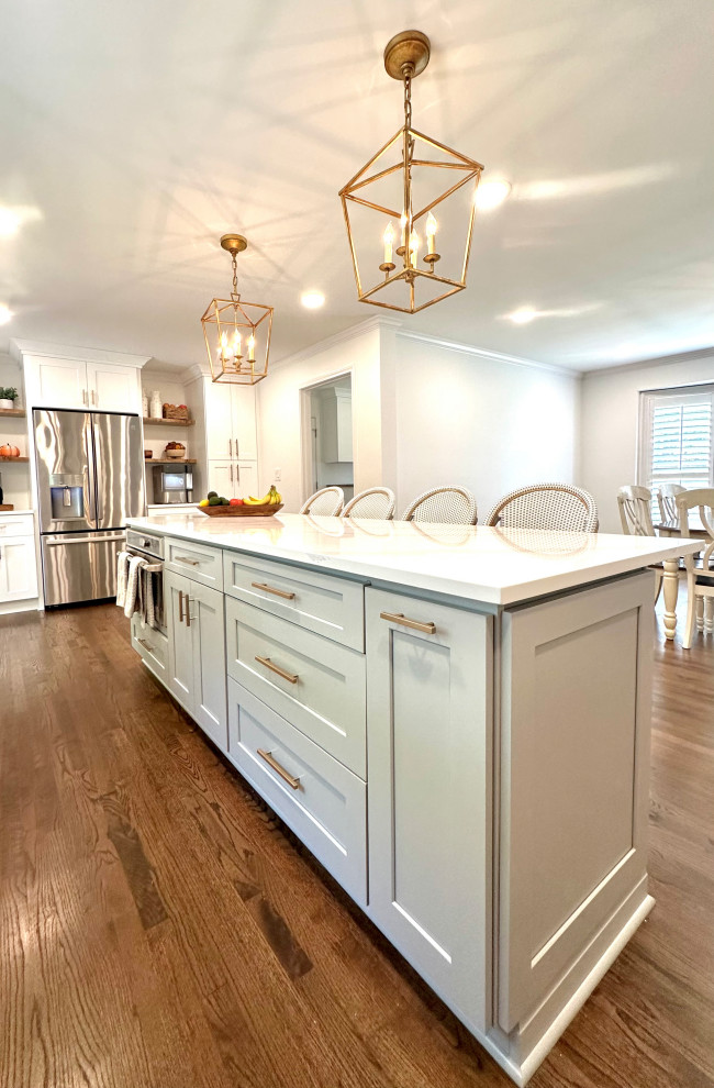 Inspiration for a large contemporary single-wall open plan kitchen in Atlanta with a drop-in sink, flat-panel cabinets, white cabinets, quartz benchtops, white splashback, subway tile splashback, stainless steel appliances, medium hardwood floors, with island, brown floor, white benchtop and vaulted.