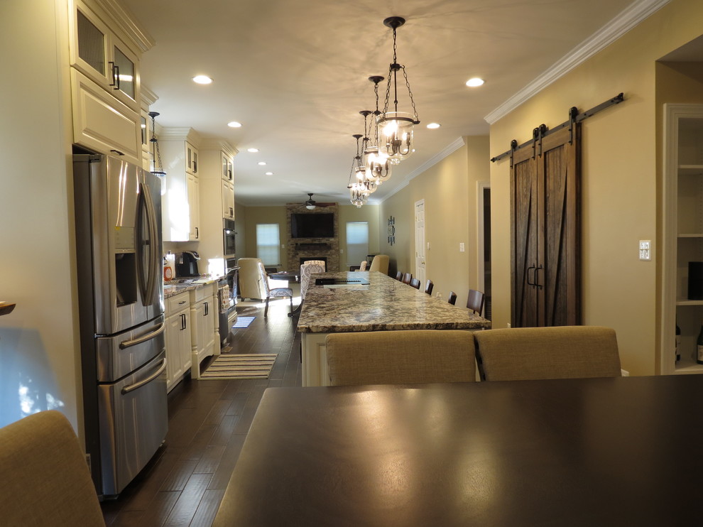 Large transitional galley dark wood floor and brown floor kitchen photo with a double-bowl sink, raised-panel cabinets, white cabinets, granite countertops, white backsplash, porcelain backsplash, stainless steel appliances and an island