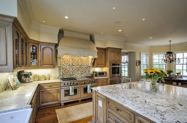 Expansive traditional u-shaped eat-in kitchen in San Francisco with a farmhouse sink, beige cabinets, limestone benchtops, multi-coloured splashback, stainless steel appliances, limestone floors and with island.