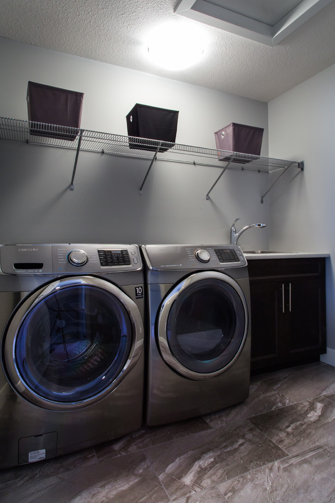 Photo of a small contemporary single-wall dedicated laundry room in Edmonton with a single-bowl sink, shaker cabinets, dark wood cabinets, laminate benchtops, grey walls, ceramic floors and a side-by-side washer and dryer.