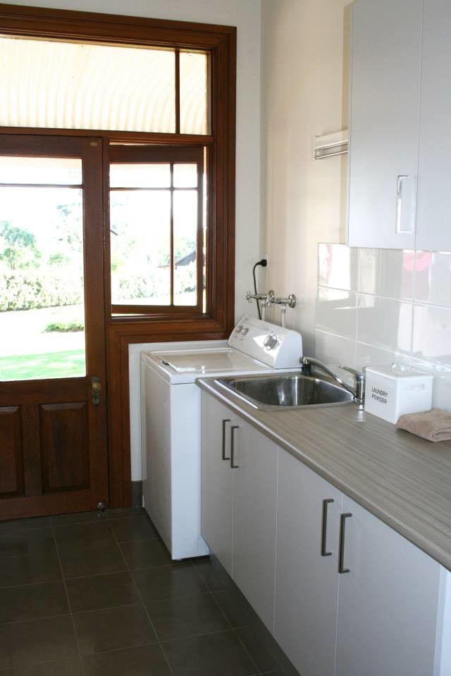 Photo of a large modern single-wall dedicated laundry room in Sydney with a drop-in sink, white cabinets, laminate benchtops, beige walls, ceramic floors, a side-by-side washer and dryer and flat-panel cabinets.