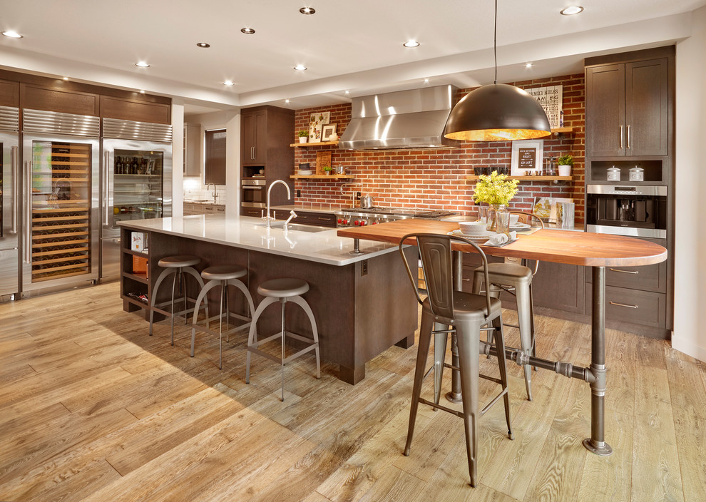Inspiration for an industrial l-shaped kitchen in Edmonton with a farmhouse sink, shaker cabinets, dark wood cabinets, red splashback, brick splashback, stainless steel appliances, medium hardwood floors, with island, brown floor and white benchtop.