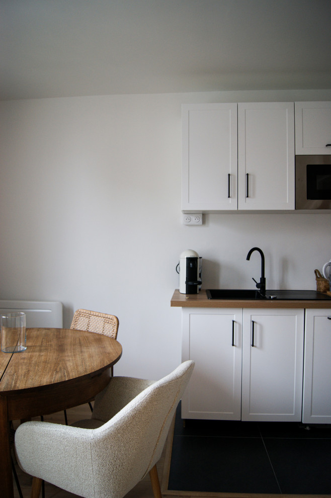 Bild på ett mellanstort funkis brun brunt kök, med en enkel diskho, släta luckor, vita skåp, träbänkskiva, vitt stänkskydd, glaspanel som stänkskydd, integrerade vitvaror, klinkergolv i keramik och svart golv