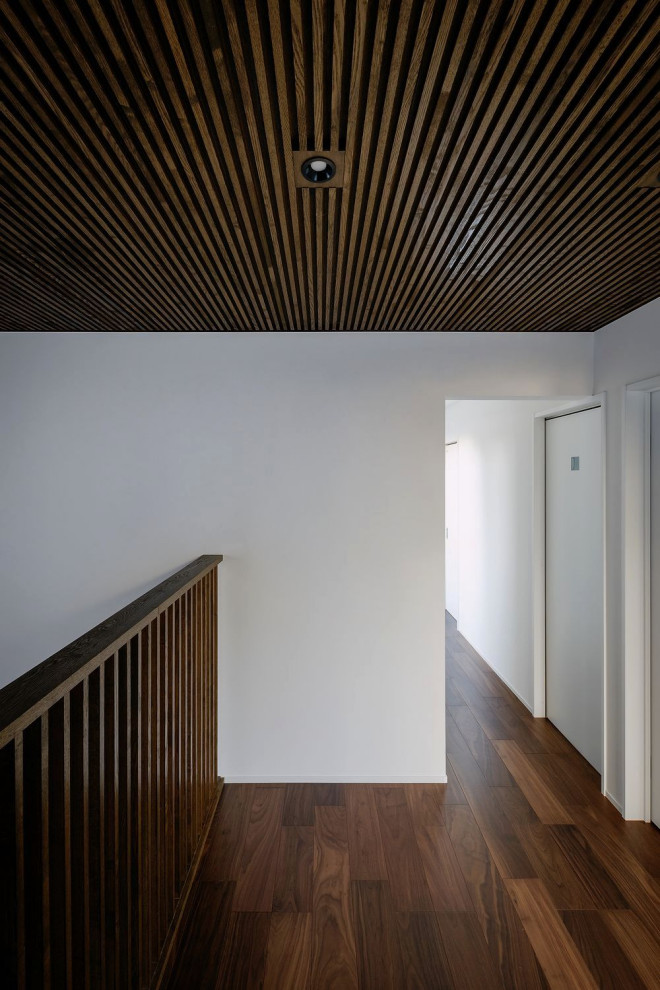 Пример оригинального дизайна: огромный коридор с белыми стенами, деревянным полом, коричневым полом, кессонным потолком и обоями на стенах