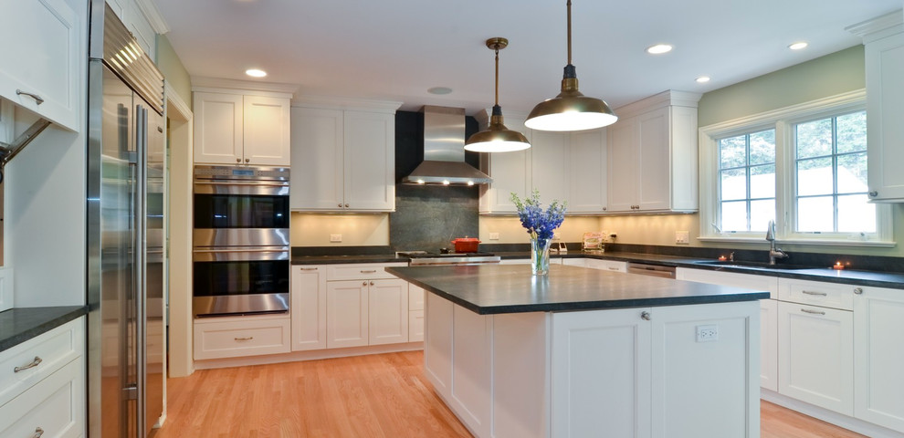 This is an example of a mid-sized transitional u-shaped separate kitchen in Chicago with an undermount sink, shaker cabinets, white cabinets, granite benchtops, stainless steel appliances, light hardwood floors and with island.