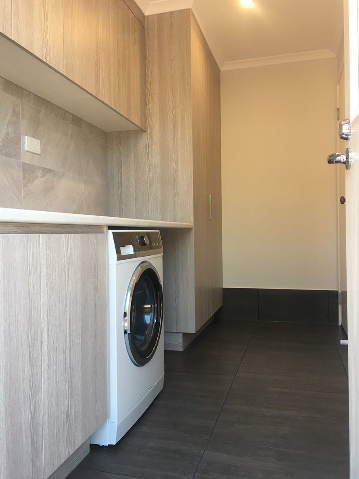 Small modern single-wall dedicated laundry room in Brisbane with a drop-in sink, flat-panel cabinets, light wood cabinets, laminate benchtops, grey walls, ceramic floors, an integrated washer and dryer, black floor and grey benchtop.