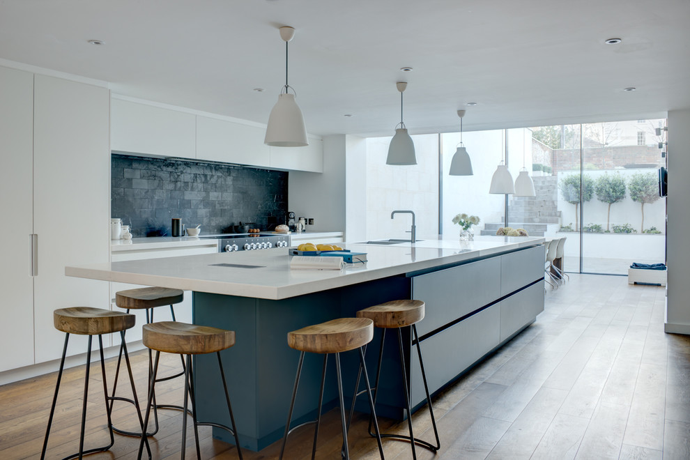Inspiration for an expansive contemporary single-wall open plan kitchen in London with an integrated sink, flat-panel cabinets, white cabinets, quartzite benchtops, black splashback, marble splashback, panelled appliances, medium hardwood floors, with island, beige floor and white benchtop.
