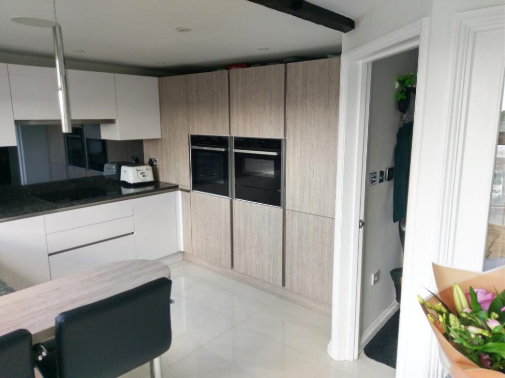 Photo of a small modern u-shaped eat-in kitchen in London with an integrated sink, flat-panel cabinets, granite benchtops, metallic splashback, glass sheet splashback, stainless steel appliances, ceramic floors, a peninsula, beige floor and black benchtop.