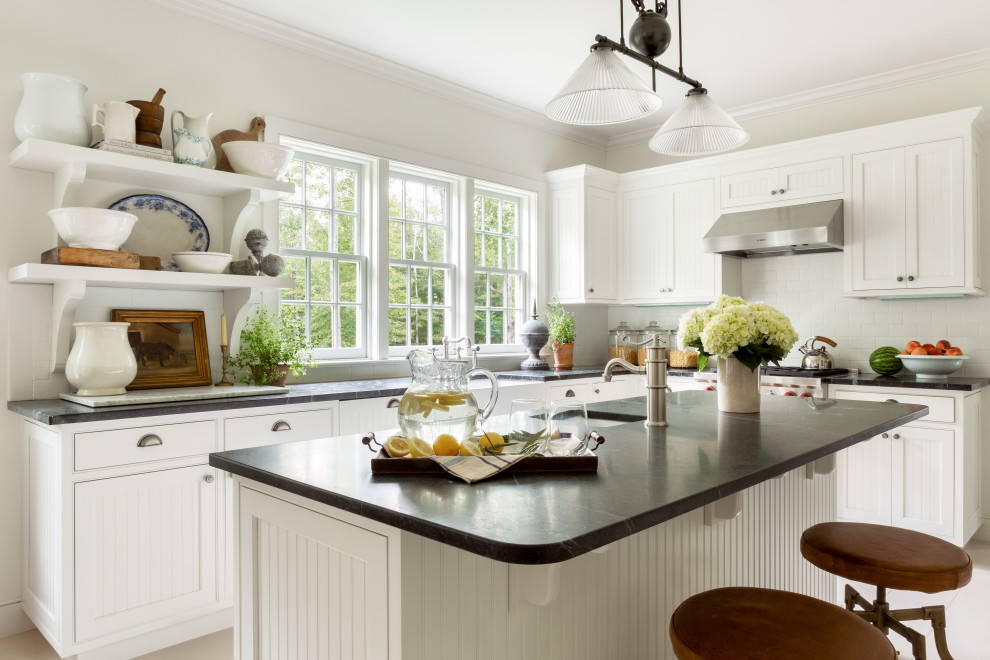 Inspiration for a country l-shaped kitchen in Bridgeport with a farmhouse sink, beaded inset cabinets, white cabinets, white splashback, subway tile splashback, stainless steel appliances, light hardwood floors, with island, beige floor and black benchtop.