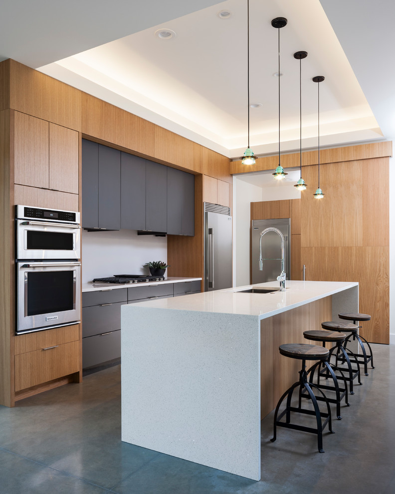 Mid-sized contemporary l-shaped open plan kitchen in Seattle with an undermount sink, flat-panel cabinets, quartz benchtops, white splashback, stone slab splashback, stainless steel appliances, concrete floors, with island, grey floor and medium wood cabinets.