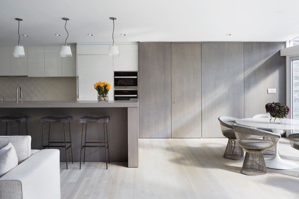 Photo of a midcentury galley open plan kitchen in New York with flat-panel cabinets, grey cabinets, beige splashback, panelled appliances, light hardwood floors and with island.