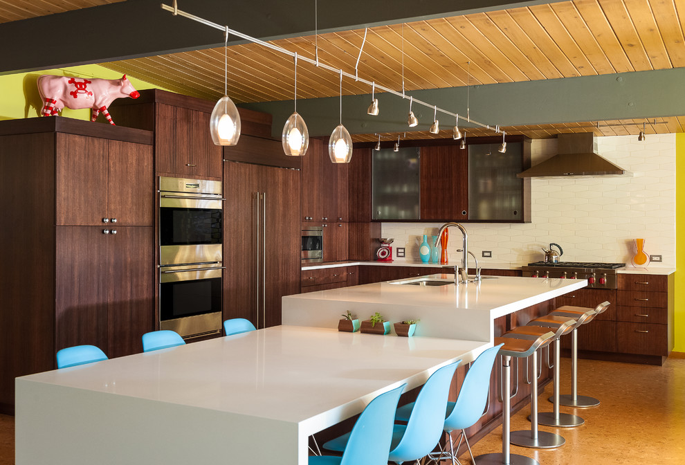 This is an example of a midcentury galley open plan kitchen in Portland with an undermount sink, flat-panel cabinets, dark wood cabinets, stainless steel appliances, cork floors, quartzite benchtops, white splashback, ceramic splashback, with island, white benchtop and wood.