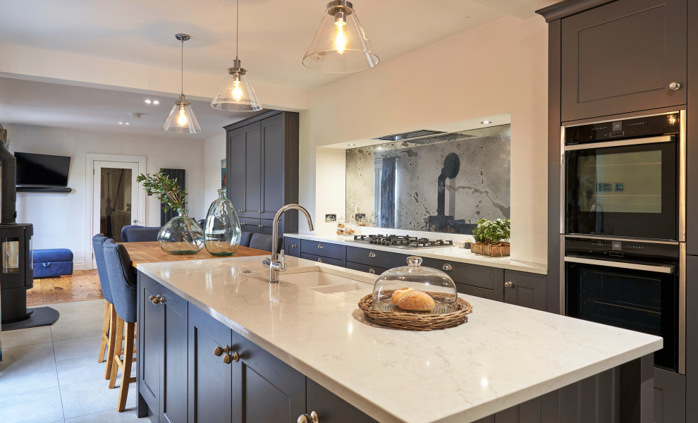 Photo of a mid-sized traditional galley eat-in kitchen in Belfast with a farmhouse sink, shaker cabinets, grey cabinets, quartzite benchtops, metallic splashback, glass sheet splashback, black appliances, ceramic floors, with island, beige floor and yellow benchtop.