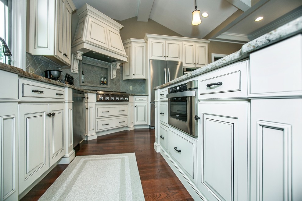 Design ideas for a large traditional kitchen in St Louis with an undermount sink, raised-panel cabinets, white cabinets, granite benchtops, beige splashback, ceramic splashback, stainless steel appliances, dark hardwood floors and with island.