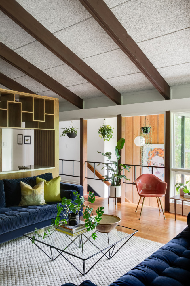 Пример оригинального дизайна: большая открытая гостиная комната в стиле ретро с белыми стенами, светлым паркетным полом, коричневым полом, балками на потолке, сводчатым потолком и синим диваном без камина