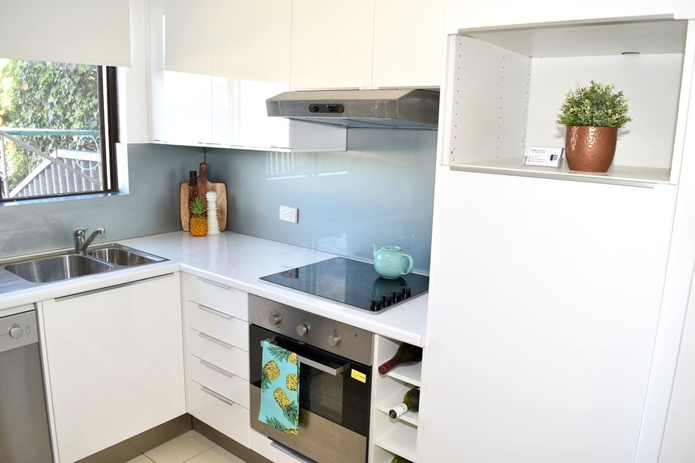 Small contemporary u-shaped kitchen in Perth with a double-bowl sink, flat-panel cabinets, white cabinets, laminate benchtops, blue splashback, glass sheet splashback, stainless steel appliances and porcelain floors.