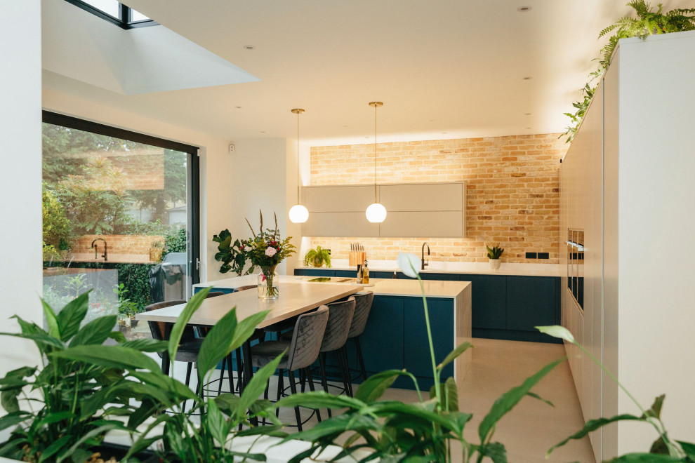 This is an example of a large transitional open plan kitchen in London with a drop-in sink, flat-panel cabinets, blue cabinets, black appliances, cement tiles, with island, grey floor, white benchtop and vaulted.