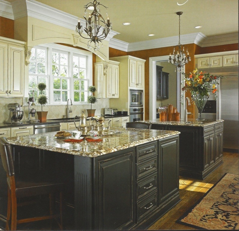 This is an example of a large traditional single-wall separate kitchen in Atlanta with an undermount sink, raised-panel cabinets, white cabinets, granite benchtops, beige splashback, travertine splashback, stainless steel appliances, dark hardwood floors, multiple islands and brown floor.