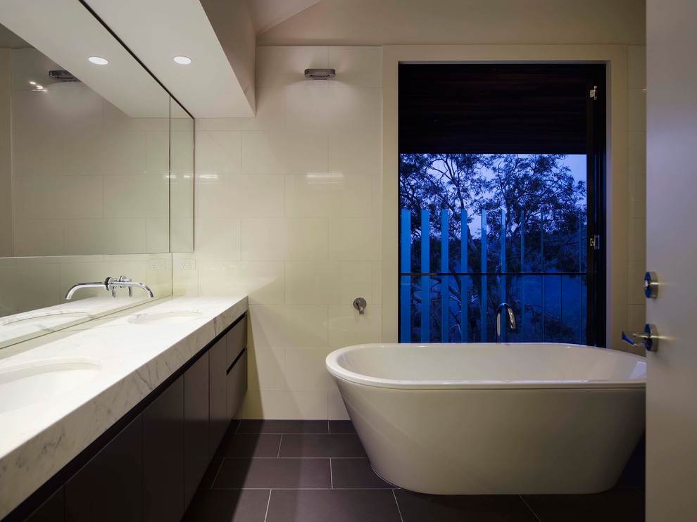 Photo of a large contemporary master bathroom in Melbourne with flat-panel cabinets, black cabinets, a freestanding tub, an open shower, a wall-mount toilet, black and white tile, ceramic tile, white walls, ceramic floors, an undermount sink and marble benchtops.