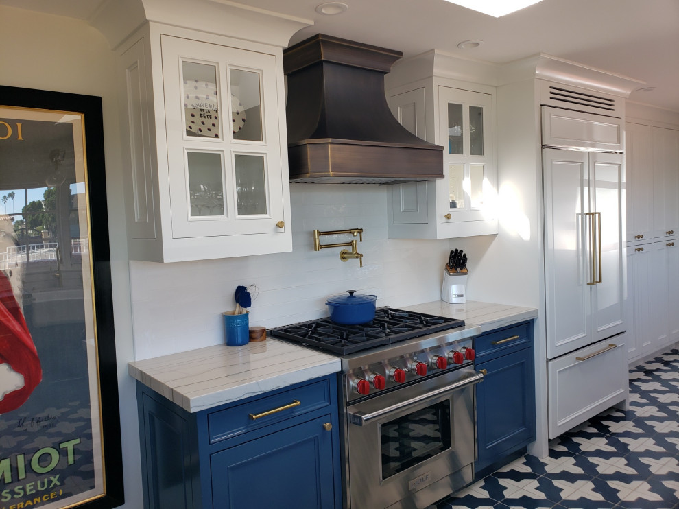 Mid-sized mediterranean kitchen pantry in San Diego with a farmhouse sink, glass-front cabinets, white cabinets, quartzite benchtops, white splashback, ceramic splashback, stainless steel appliances, porcelain floors, no island, blue floor, white benchtop and coffered.