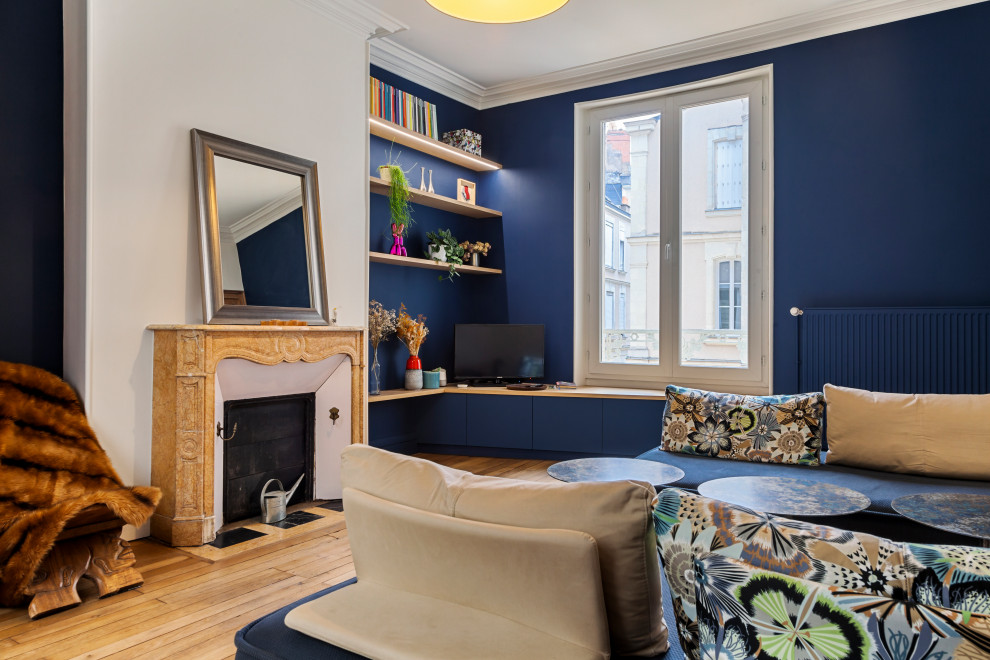 Mittelgroßes, Offenes Klassisches Wohnzimmer mit blauer Wandfarbe, hellem Holzboden und Kaminumrandung aus Stein in Angers