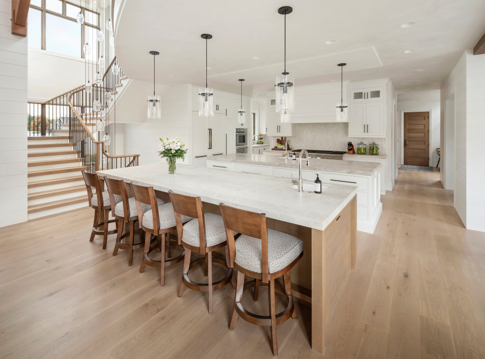Design ideas for an expansive country l-shaped open plan kitchen in Salt Lake City with a farmhouse sink, beaded inset cabinets, white cabinets, quartzite benchtops, beige splashback, limestone splashback, white appliances, light hardwood floors, multiple islands, beige floor and beige benchtop.