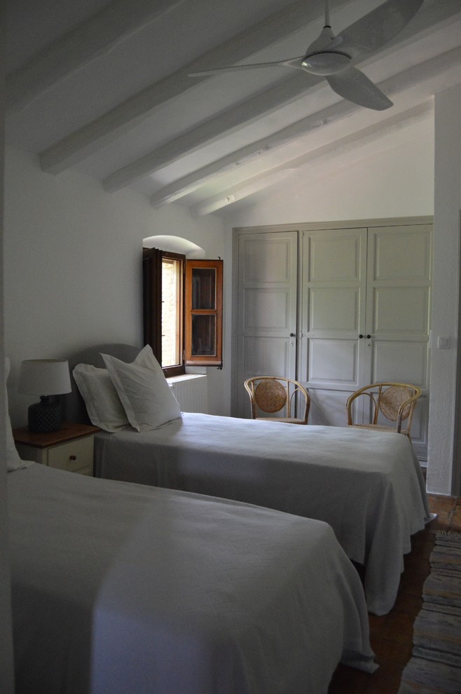 This is an example of a country guest bedroom in Barcelona with white walls and terra-cotta floors.