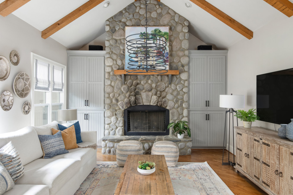 Inspiration for a classic living room in Charlotte with white walls, medium hardwood flooring, a standard fireplace, a stone fireplace surround, a wall mounted tv, brown floors, exposed beams and a vaulted ceiling.