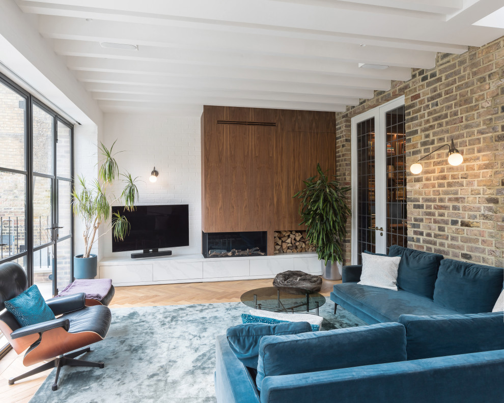 Inspiration for a transitional open concept living room in London with white walls, medium hardwood floors, a ribbon fireplace, a wood fireplace surround, a freestanding tv, brown floor, exposed beam and brick walls.